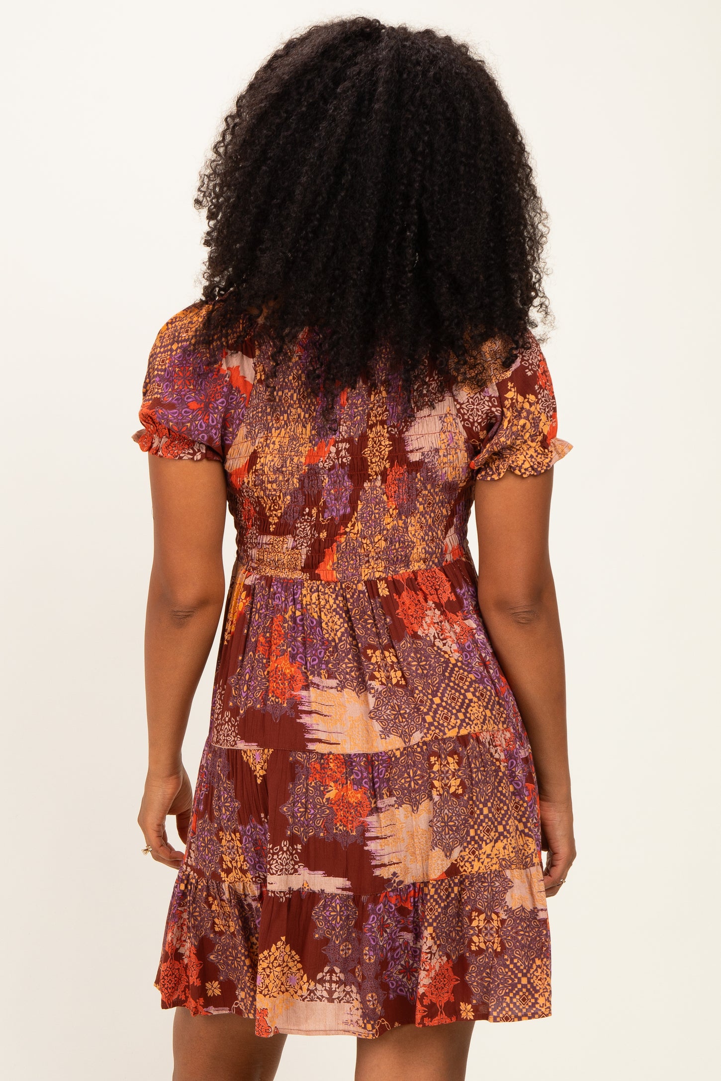 woman wearing a short-sleeve brown patterned dress with a flared skirt and a fitted bodice, seen from the back