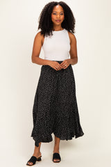 woman wearing a white sleeveless top and a black polka dot maxi skirt, standing confidently with hands clasped