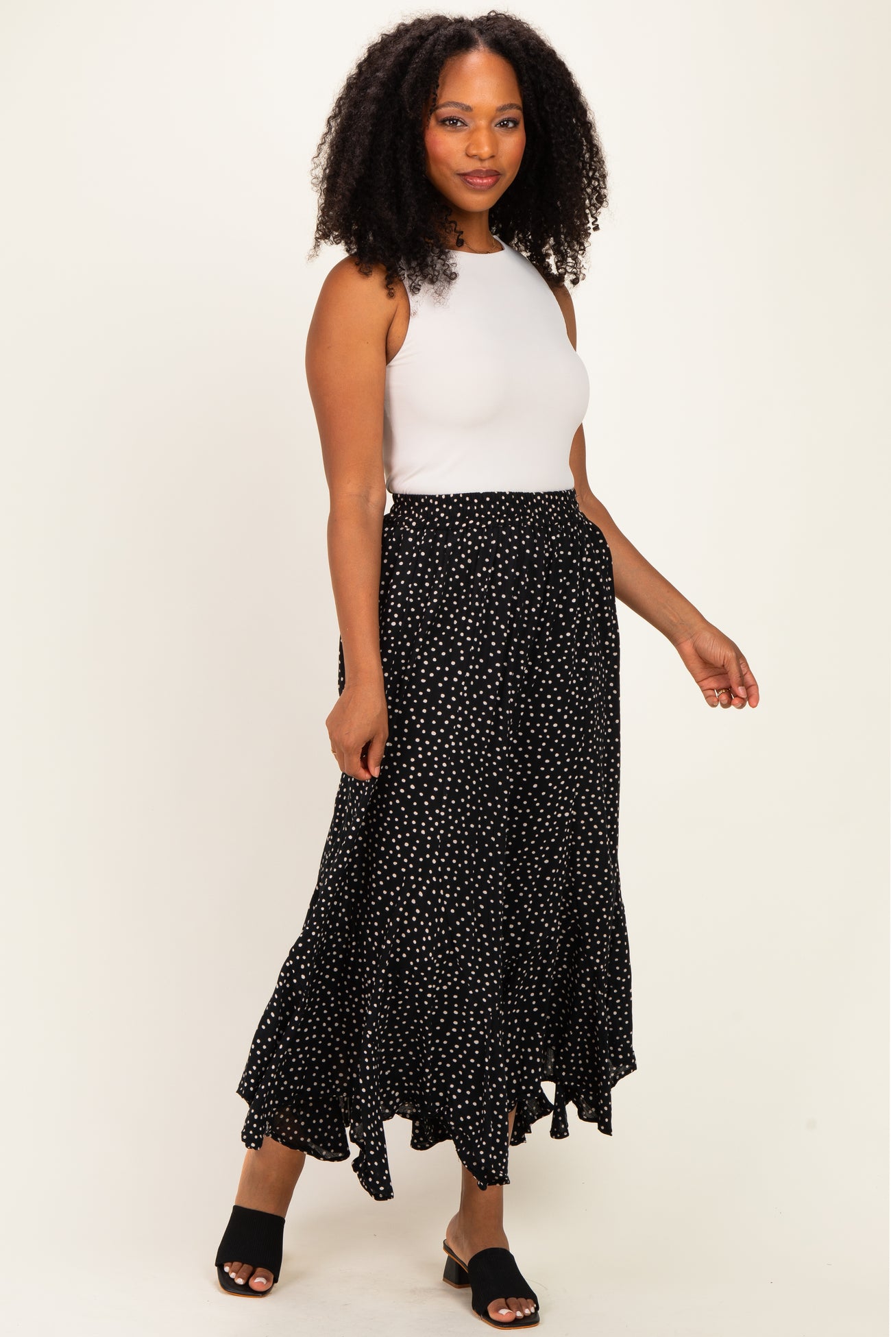 woman wearing a white sleeveless top and a black polka dot maxi skirt with a ruffled hem