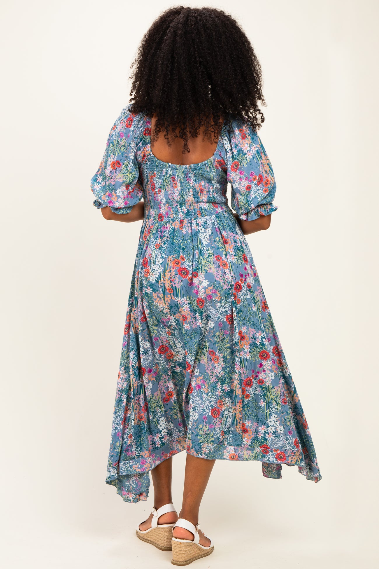 woman wearing a floral print blue maxi dress with puff sleeves and a cutout back, standing with her back to the camera
