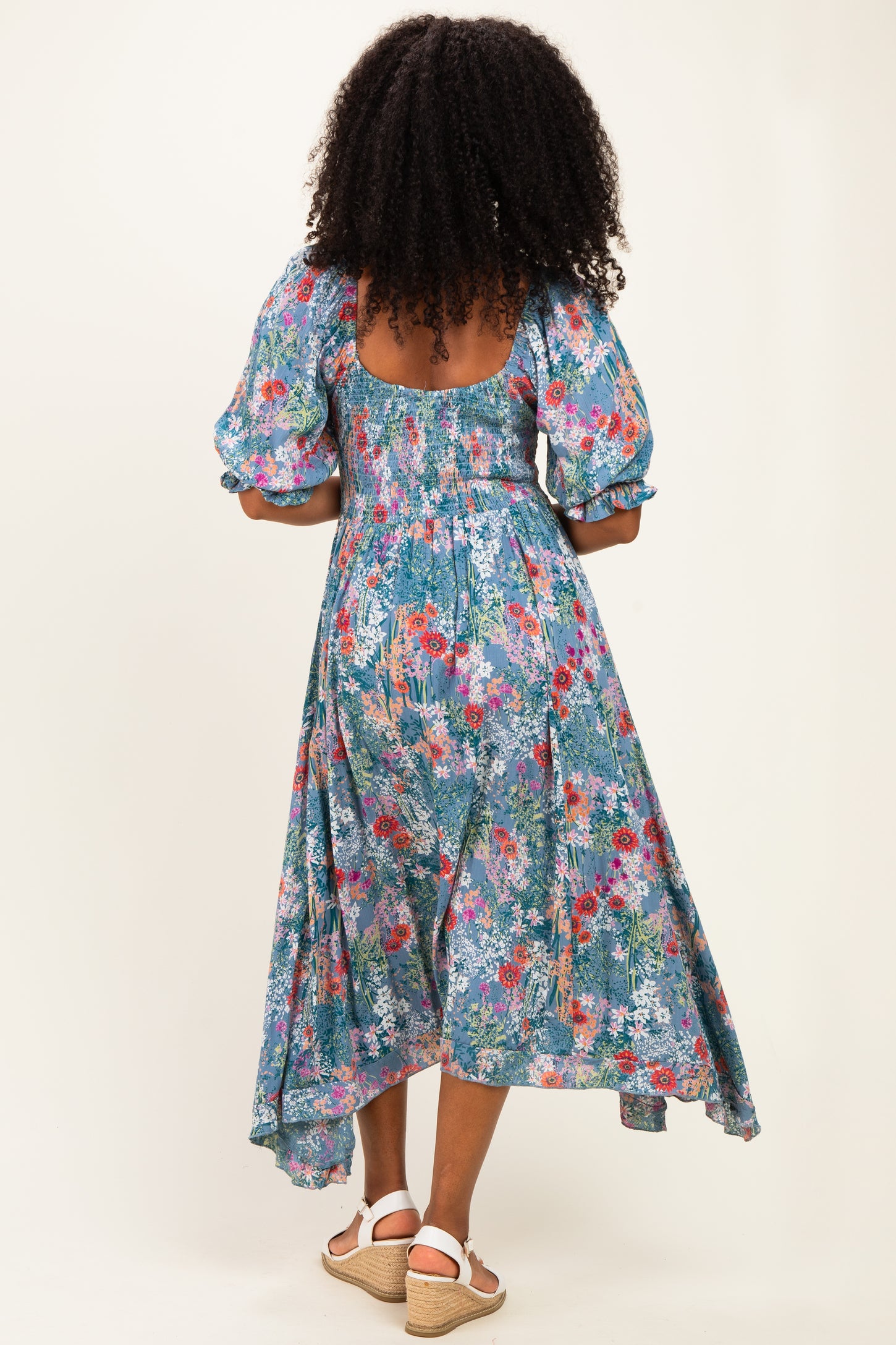 woman wearing a floral print blue maxi dress with puff sleeves and a cutout back, standing with her back to the camera