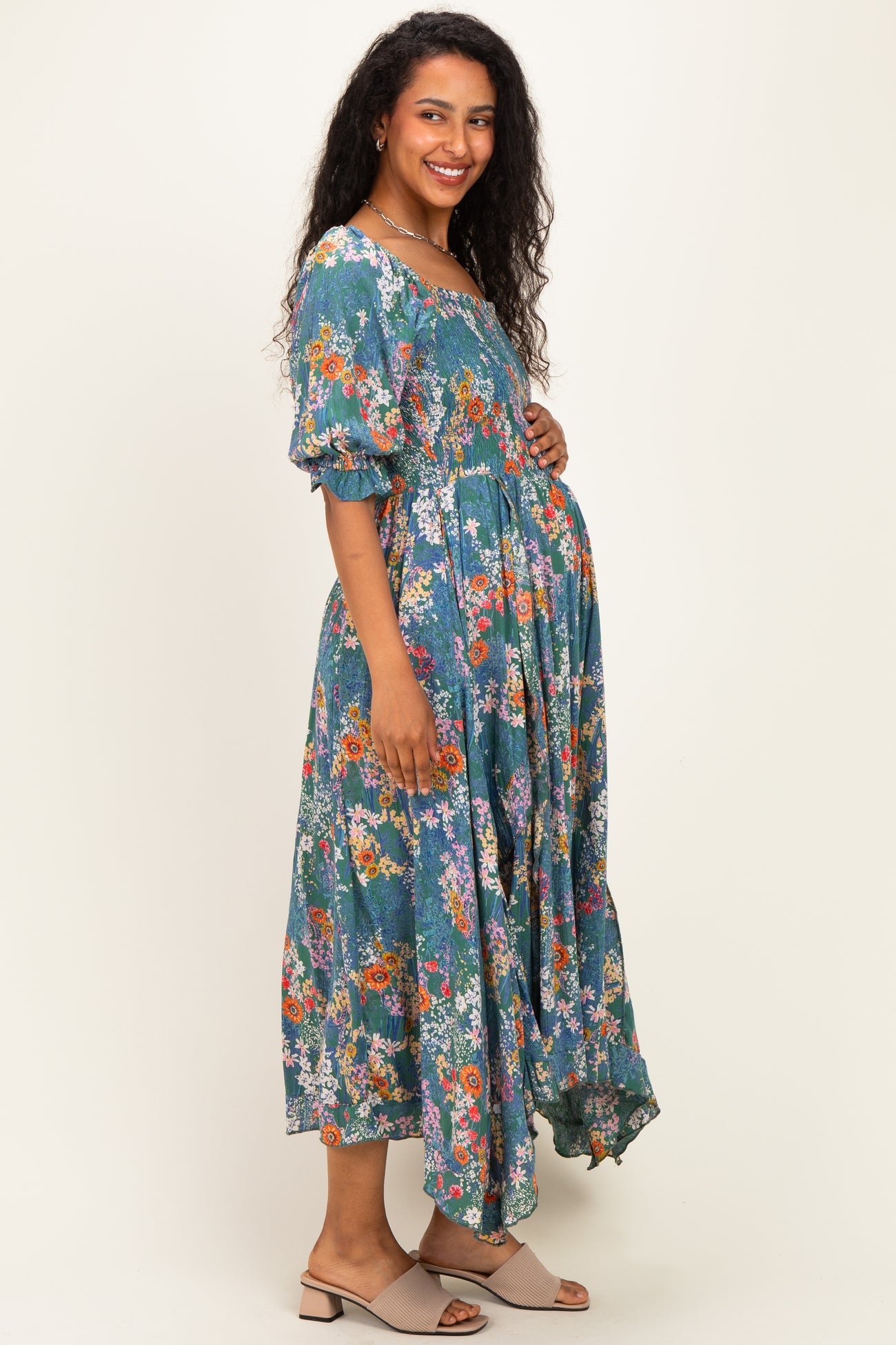 woman wearing a floral teal maternity dress with puff sleeves and a gathered waist, showing her baby bump