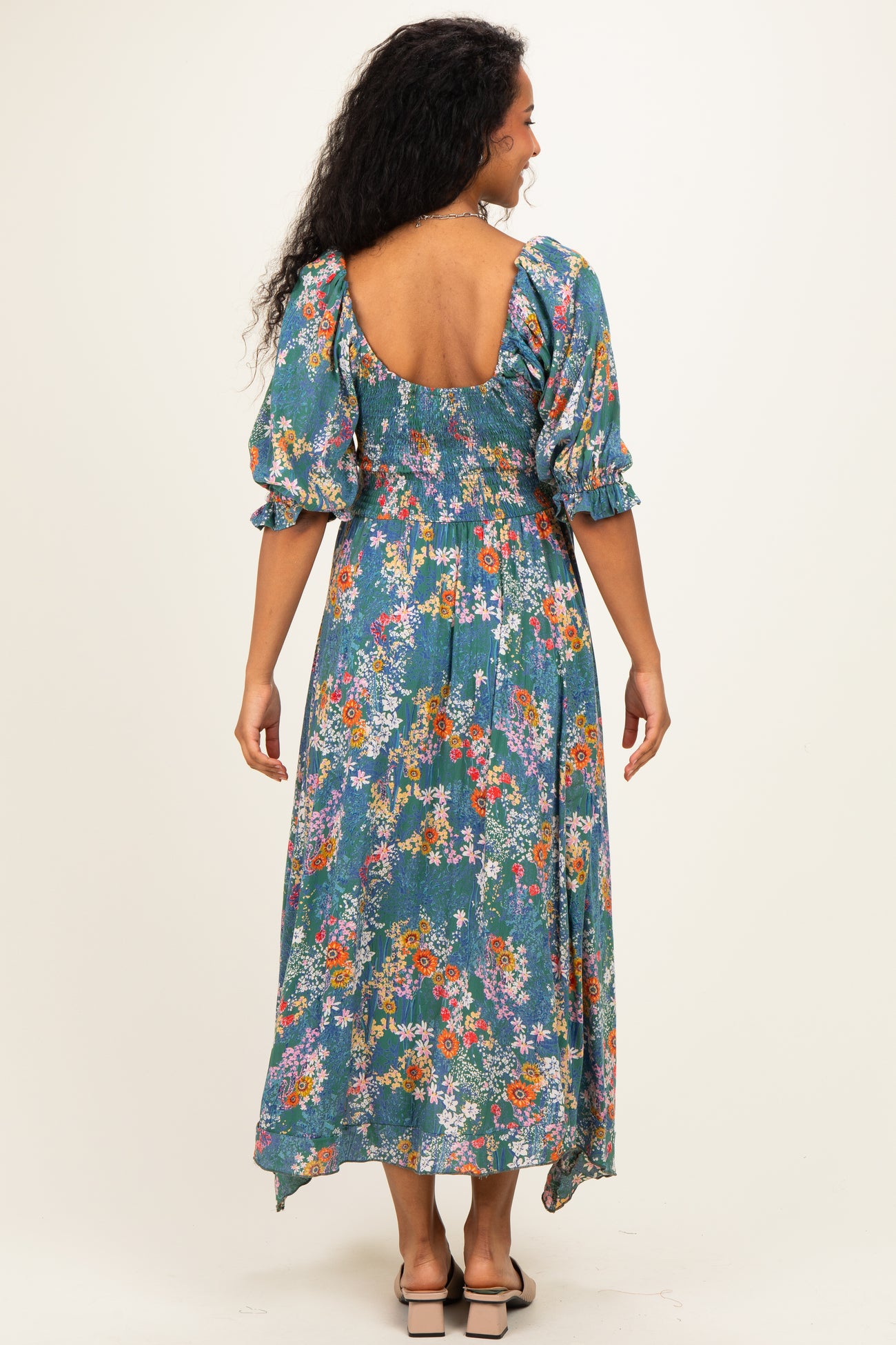 woman wearing a blue floral maternity dress with puff sleeves and a backless design, showing off her baby bump