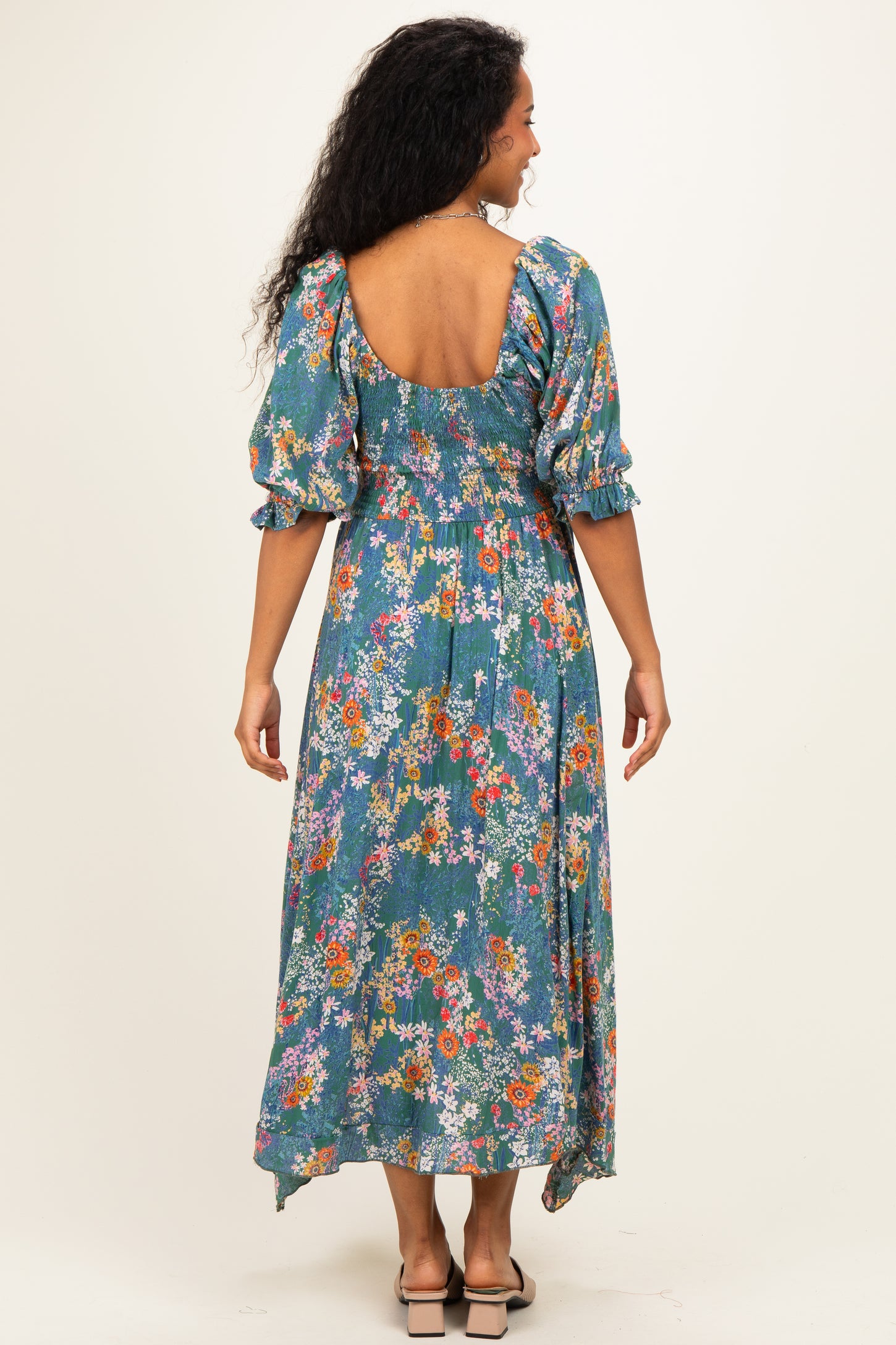 woman wearing a blue floral maternity dress with puff sleeves and a backless design, showing off her baby bump