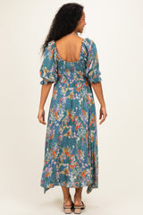 woman wearing a blue floral maternity dress with puff sleeves and a backless design, showing off her baby bump