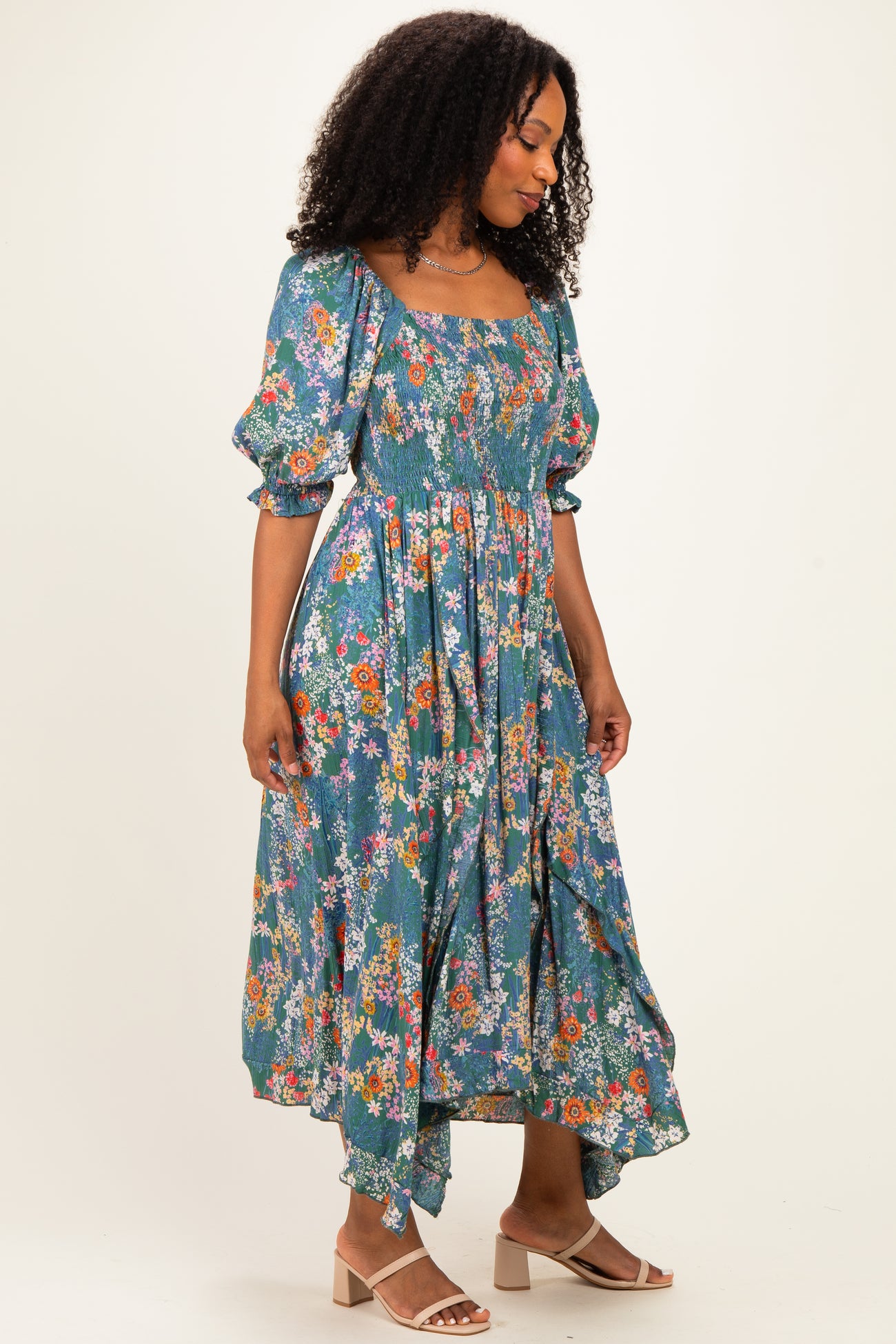 woman wearing a floral print puff sleeve midi dress in blue and green tones, standing with a slight smile