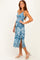 woman wearing a blue floral midi dress with a knot front and side slits, standing with one hand on her hip
