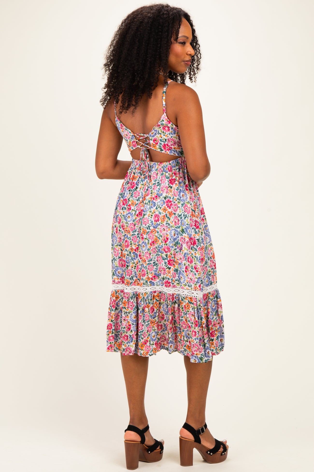woman wearing a colorful floral print dress with a back cutout and ruffled hem, standing with her back to the camera