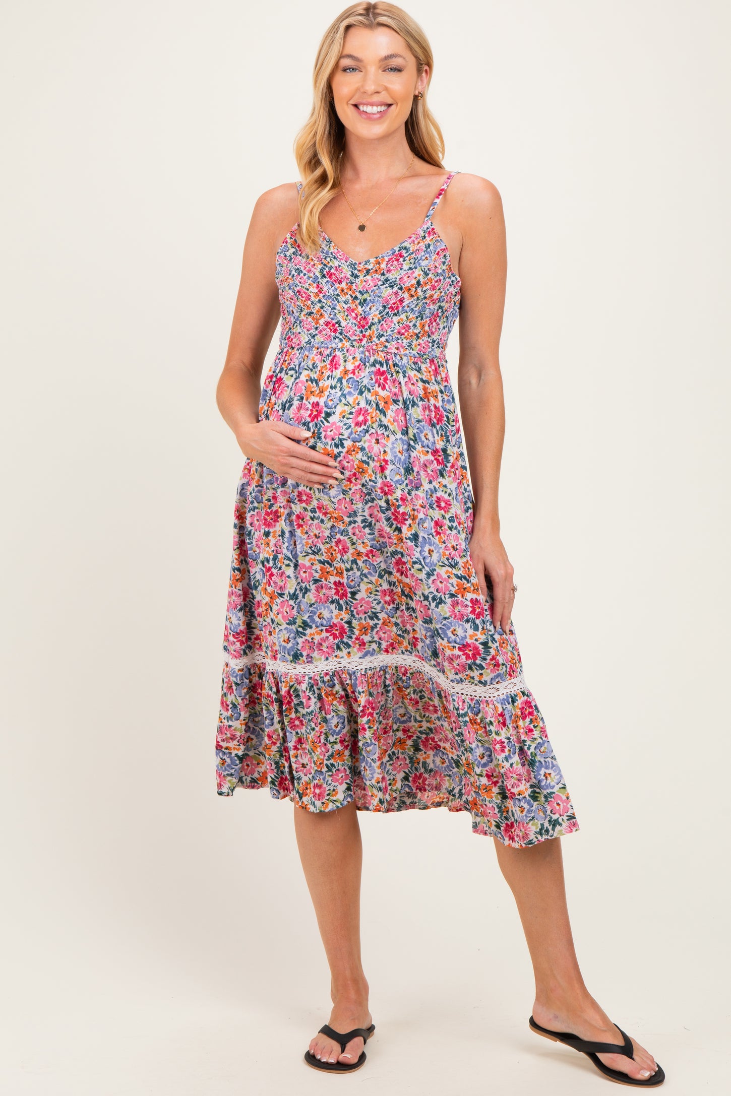 woman wearing a floral maternity dress with a smocked bodice and tiered skirt, holding her baby bump