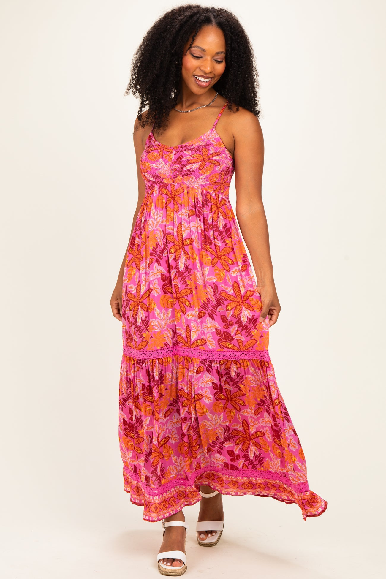 woman wearing a vibrant pink floral maxi dress with spaghetti straps and tiered skirt, smiling and standing on a plain background