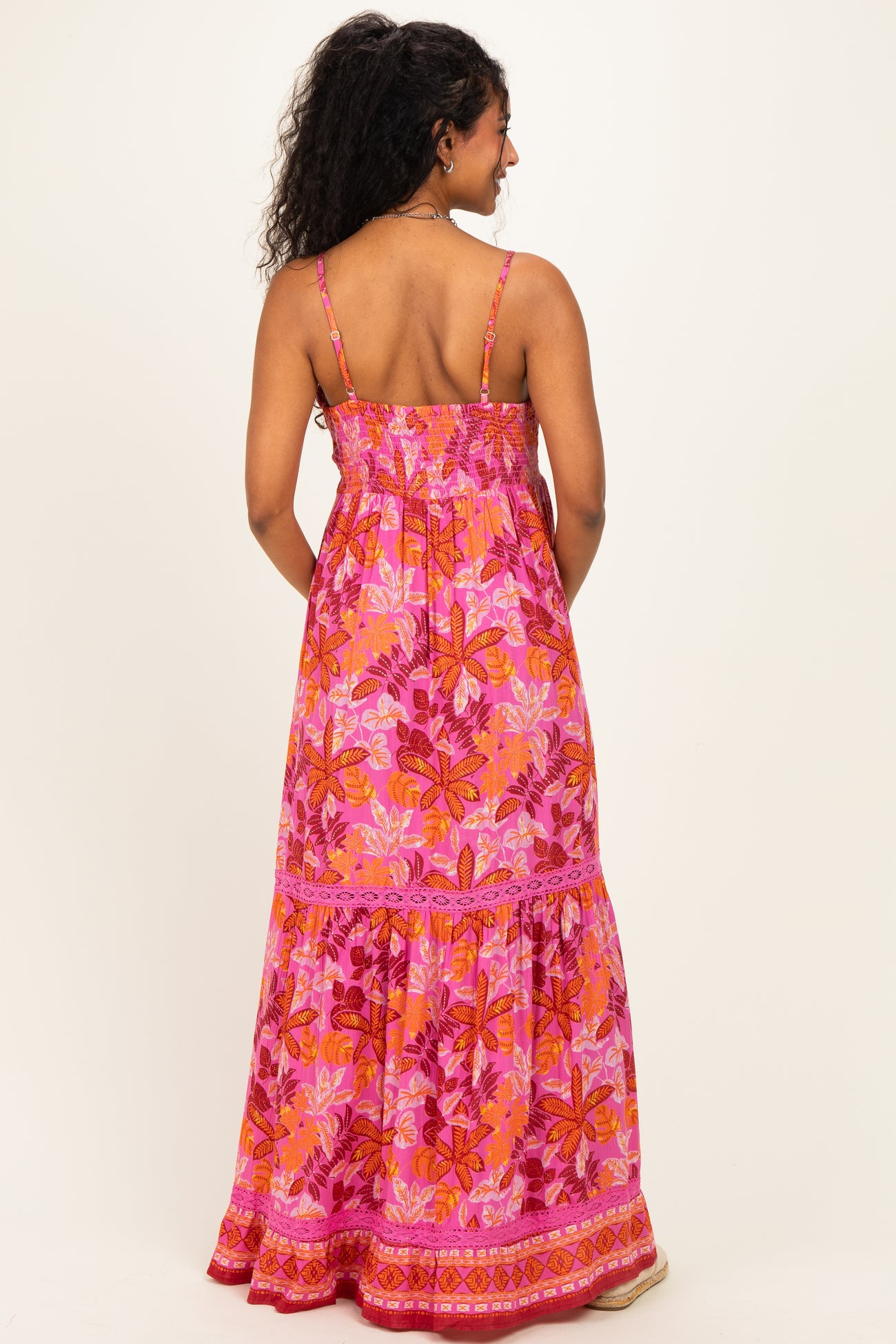 woman wearing a pink floral maternity maxi dress with adjustable straps and a tiered hem, showing her back