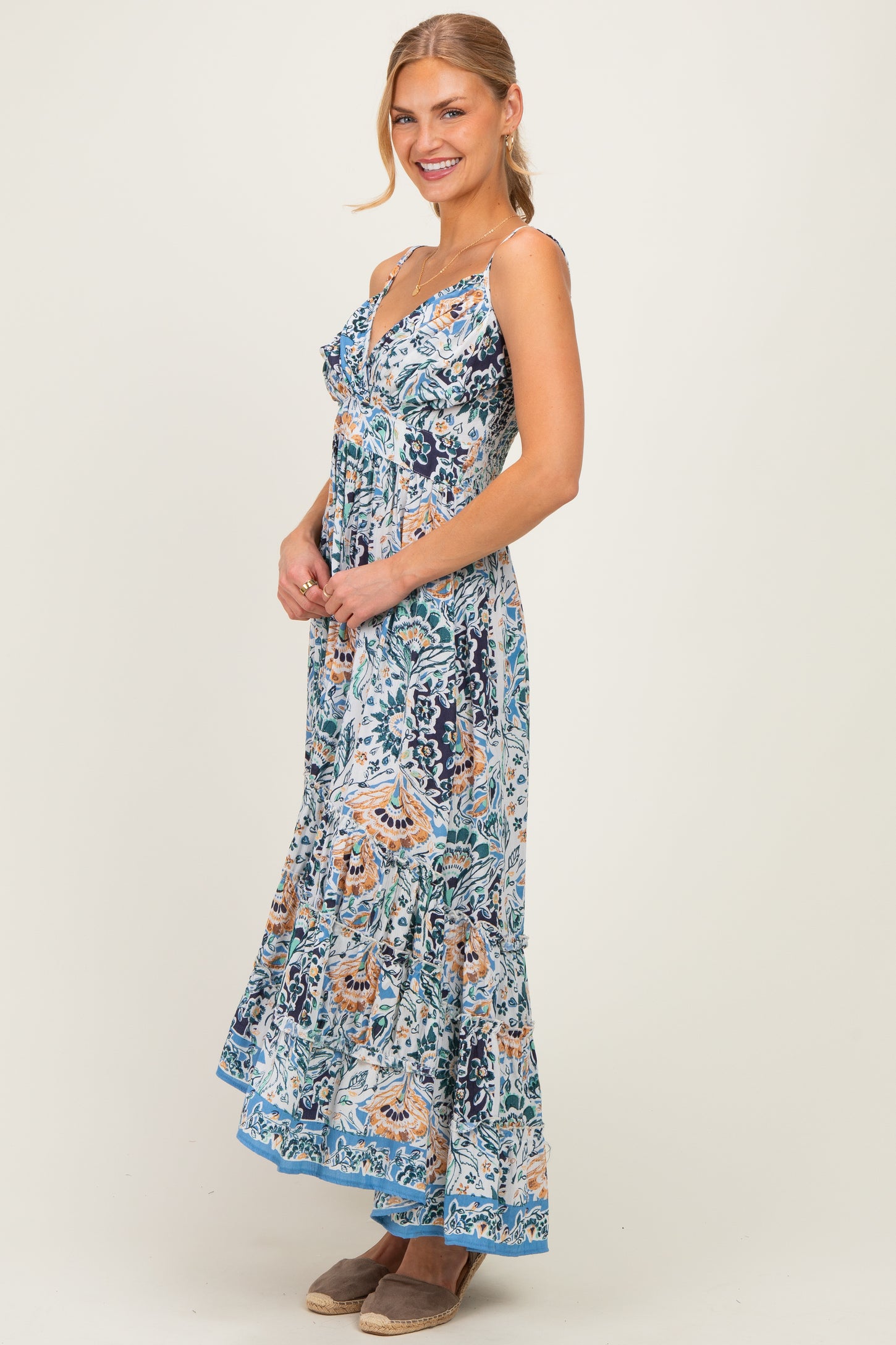 woman wearing a floral maxi dress with spaghetti straps and a flared hem, smiling and standing sideways