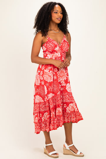 woman wearing a red floral midi dress with a v-neckline and tiered hem, paired with white wedge sandals