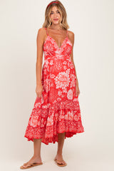 woman wearing a red floral maternity dress with a flared skirt and spaghetti straps, showcasing her baby bump