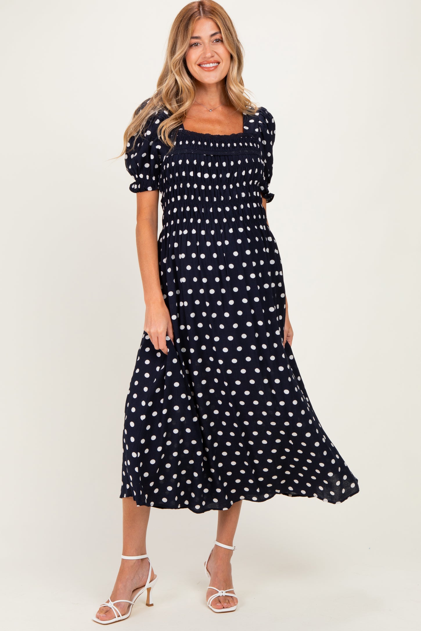 woman wearing a navy blue polka dot maternity dress with a smocked bodice and short puff sleeves, showing a baby bump