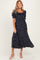 woman wearing a navy blue polka dot maternity dress with a smocked bodice and short puff sleeves, showing a baby bump