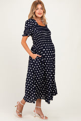 woman wearing a navy blue polka dot maternity dress with short puff sleeves and pockets, highlighting her baby bump