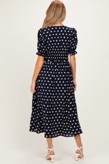 woman wearing a navy blue polka dot maternity dress with a cinched waist and short sleeves, showing off a baby bump