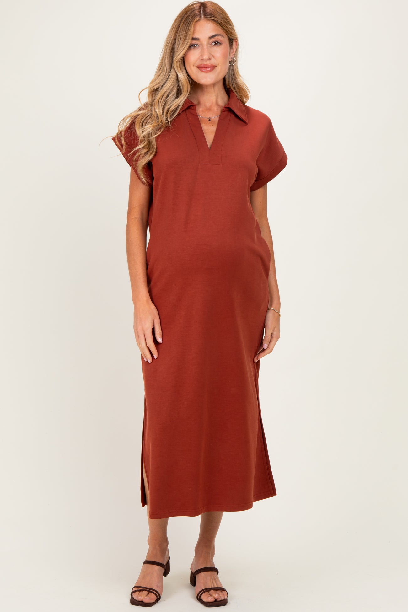 woman wearing a rust-colored maternity midi dress with a collar and side slits, showcasing her baby bump