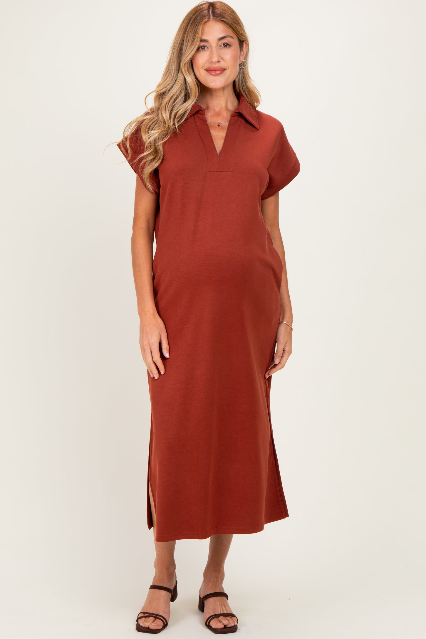woman wearing a rust-colored maternity midi dress with a collar and side slits, showcasing her baby bump