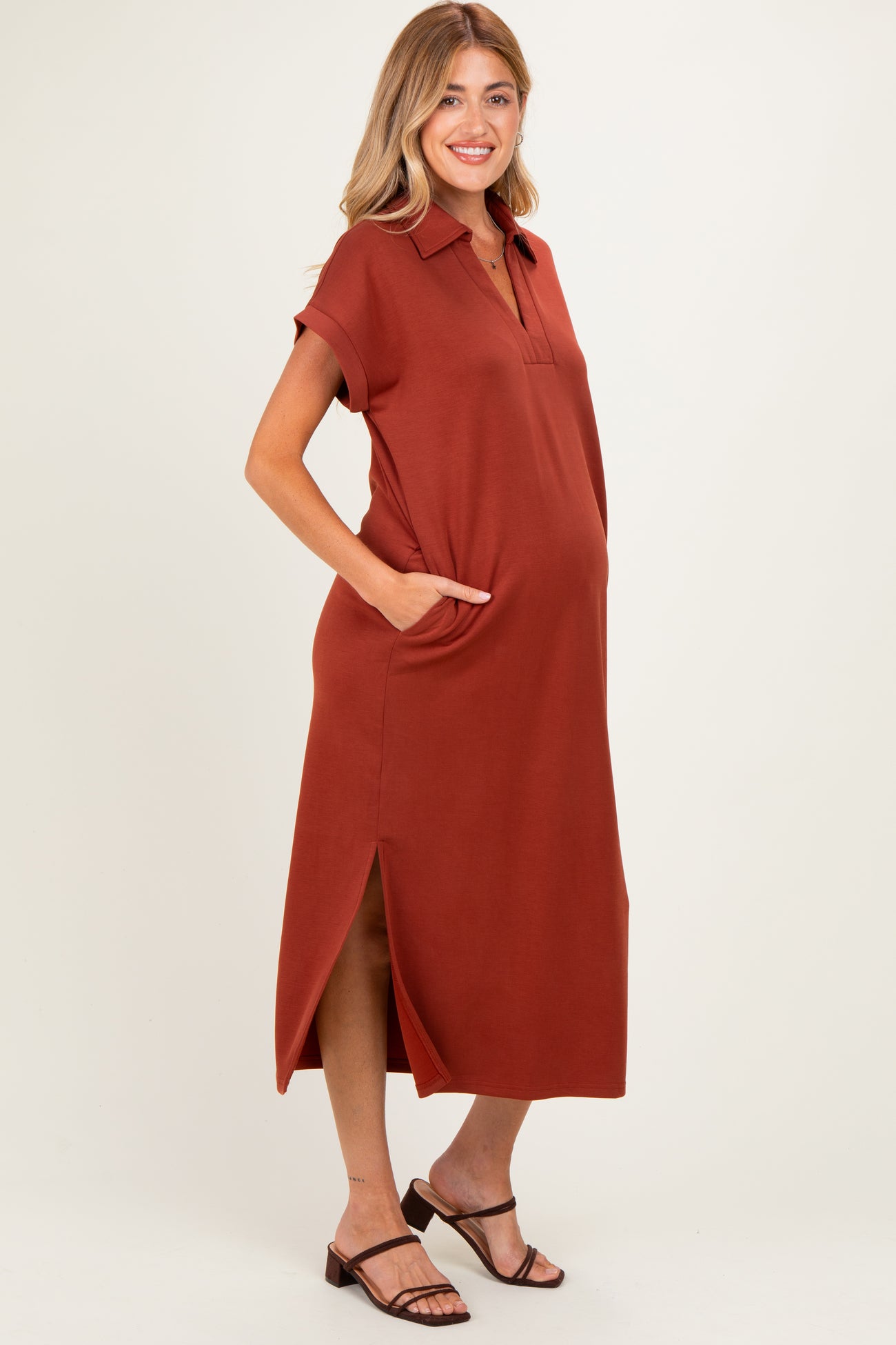 woman wearing a rust-colored maternity polo dress with pockets and side slits, showcasing her baby bump