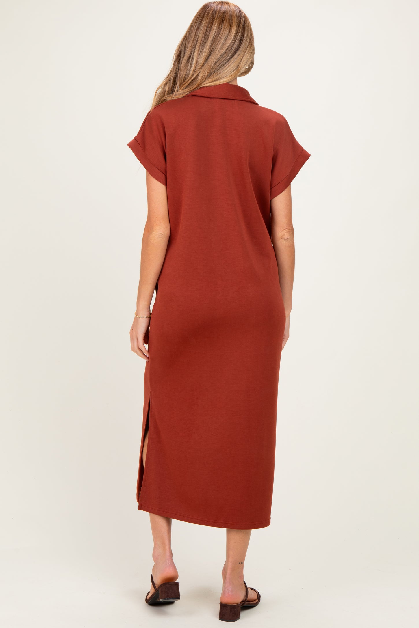 woman wearing a rust-colored maternity maxi dress with short sleeves and side slits, seen from the back