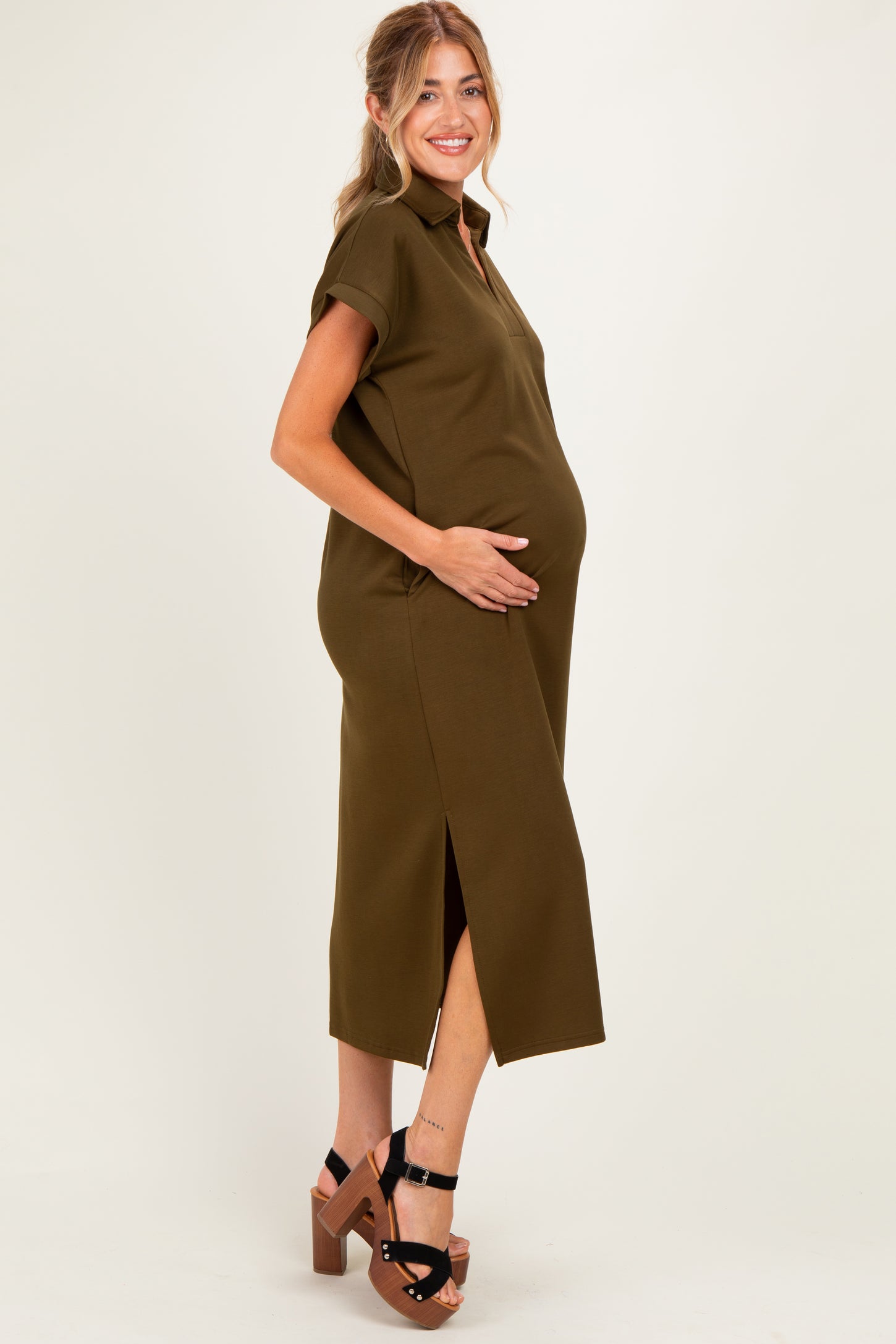 woman wearing an olive green maternity midi dress with short sleeves and side slits, cradling her baby bump