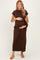 woman wearing a brown maternity dress with a side tie, holding her baby bump, standing against a neutral background