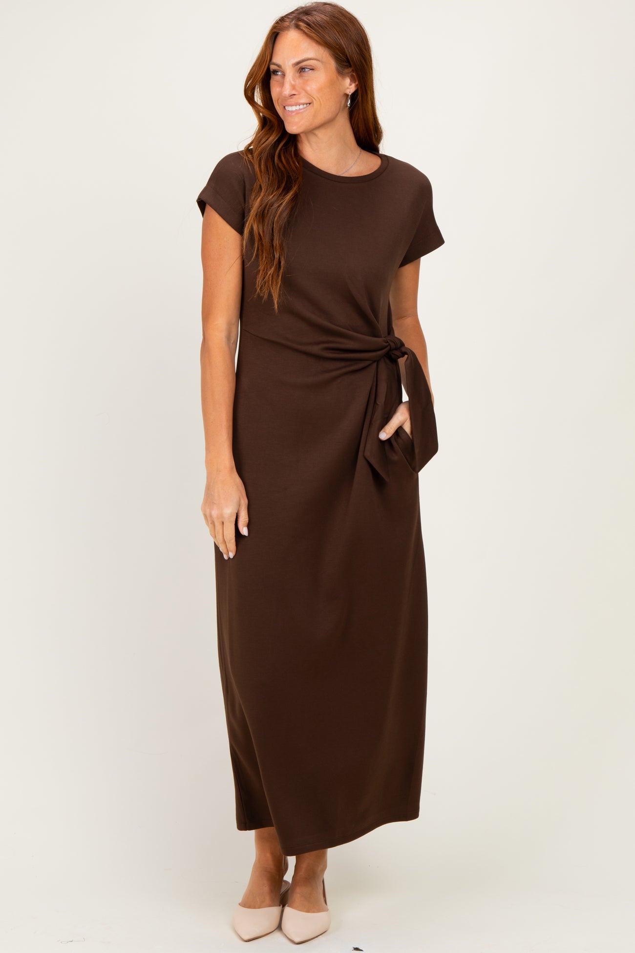 woman wearing a chocolate brown cap sleeve maxi dress with a side tie detail and a pocket