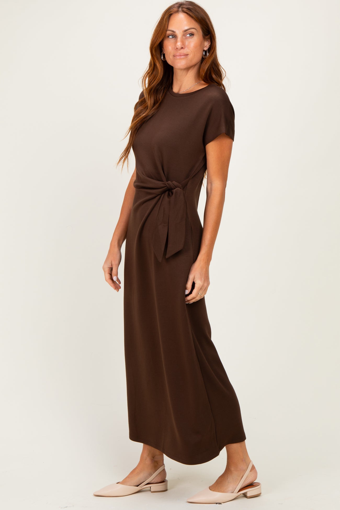 woman wearing a brown maxi dress with a tied waist and short sleeves, standing casually
