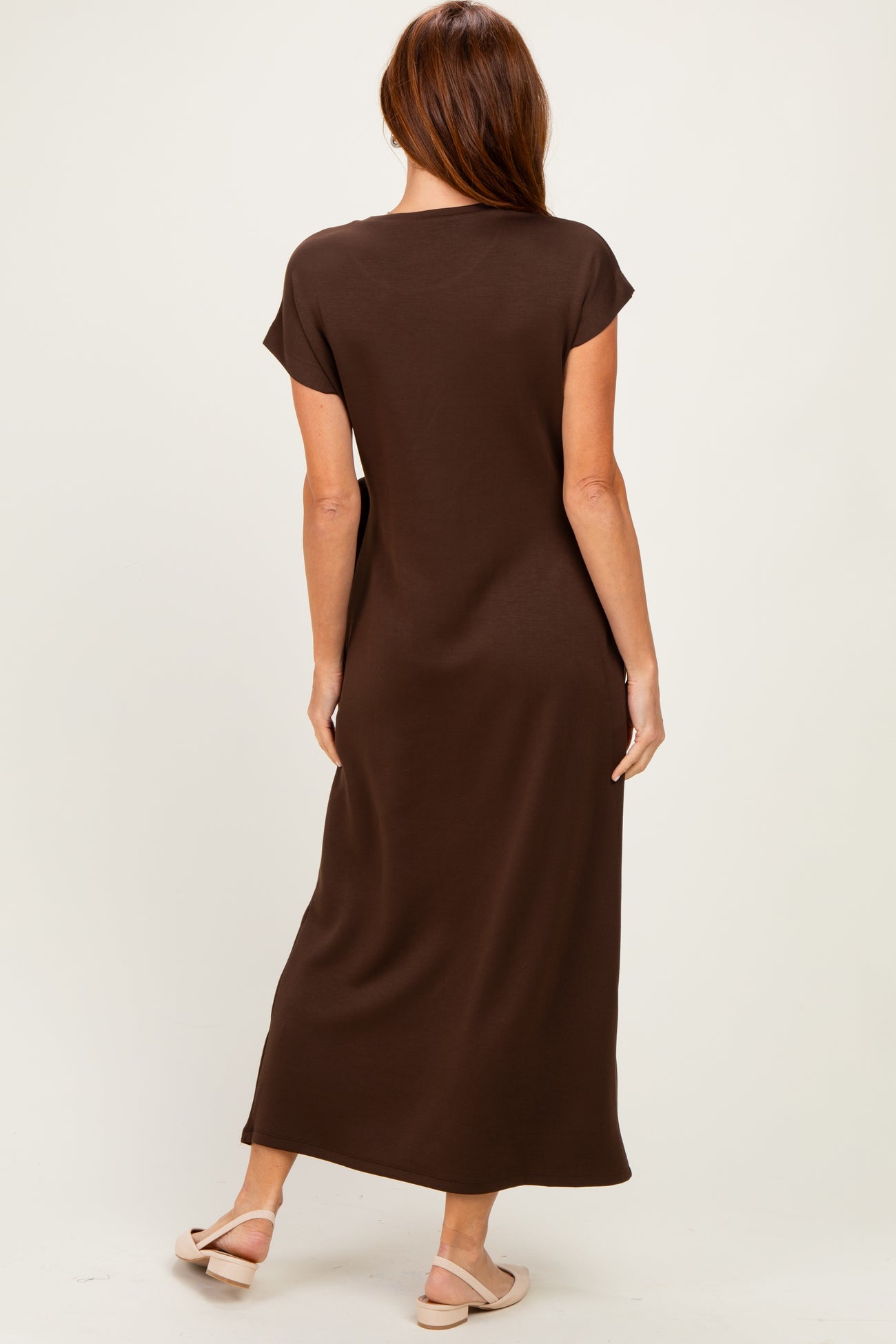 woman wearing a brown short sleeve maxi dress, seen from the back, standing in relaxed pose
