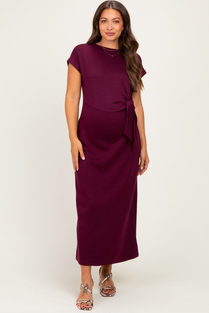 woman wearing a burgundy maternity maxi dress with a tie detail at the waist and short sleeves, showcasing her baby bump