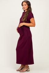 woman wearing a dark burgundy maternity maxi dress with a fitted silhouette and a visible baby bump