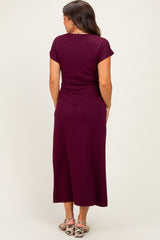 woman wearing a burgundy maternity maxi dress with short sleeves and a fitted bodice, showing a slight baby bump