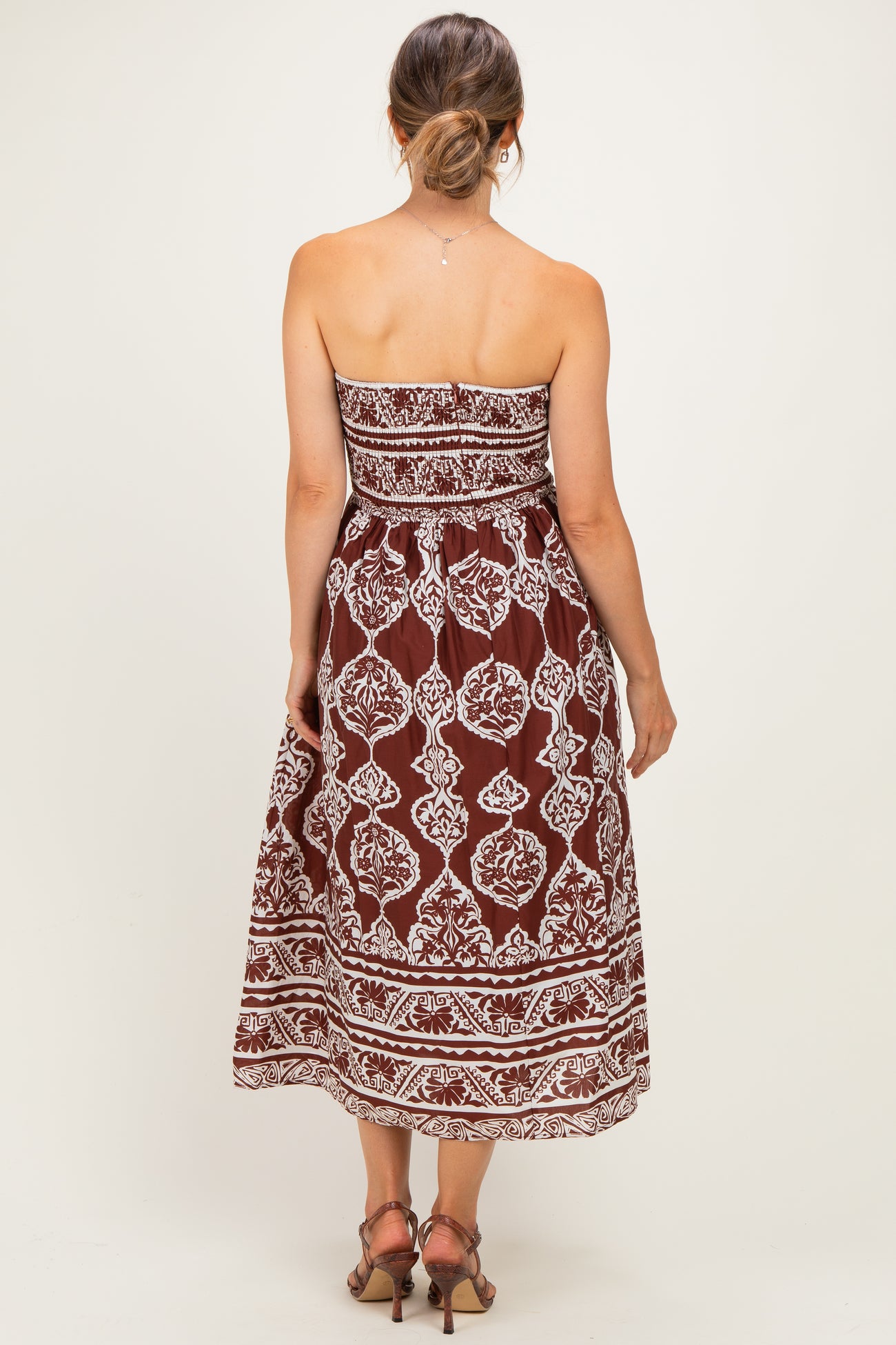 woman wearing a brown strapless maternity maxi dress with white floral patterns, showing her baby bump