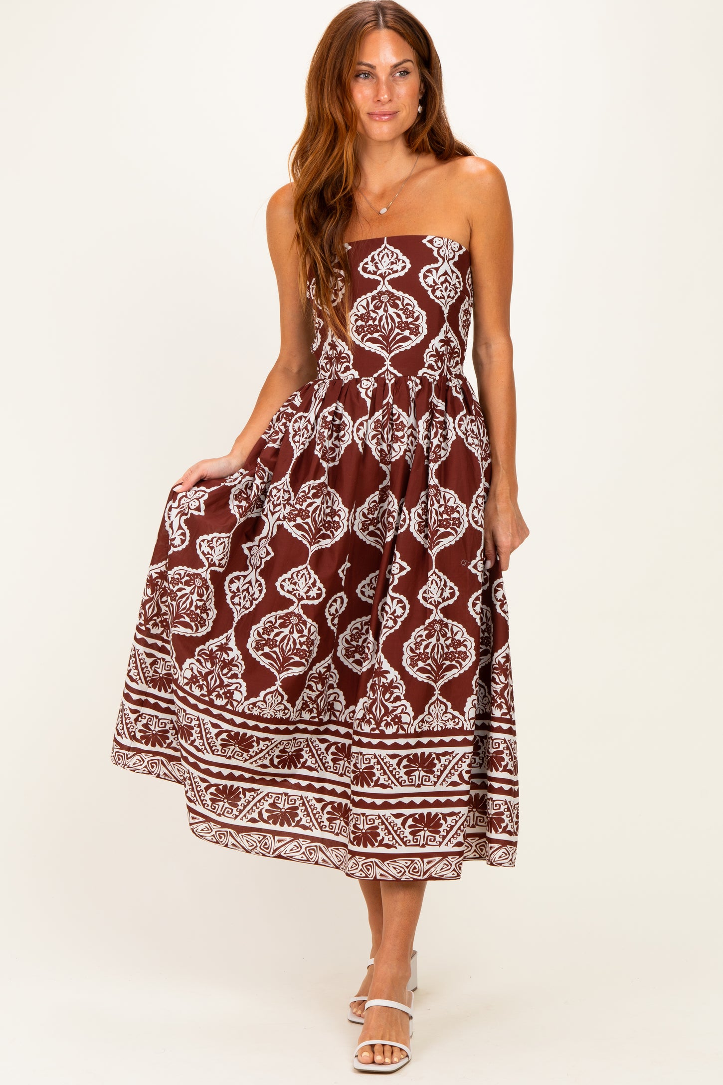 woman wearing a brown spaghetti strap maxi dress with white floral patterns and a tiered skirt