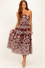 woman wearing a brown spaghetti strap maxi dress with white floral patterns and a tiered skirt