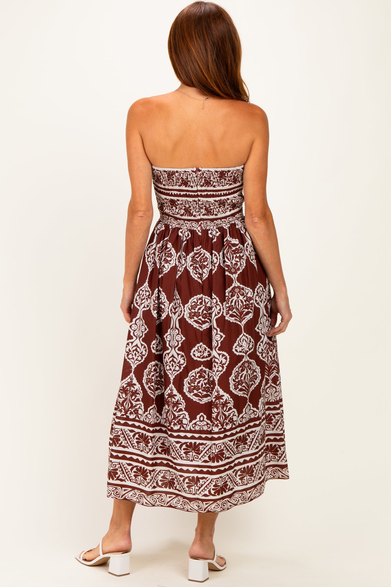 woman wearing a strapless brown and white patterned maxi dress with a fitted bodice and flowy skirt
