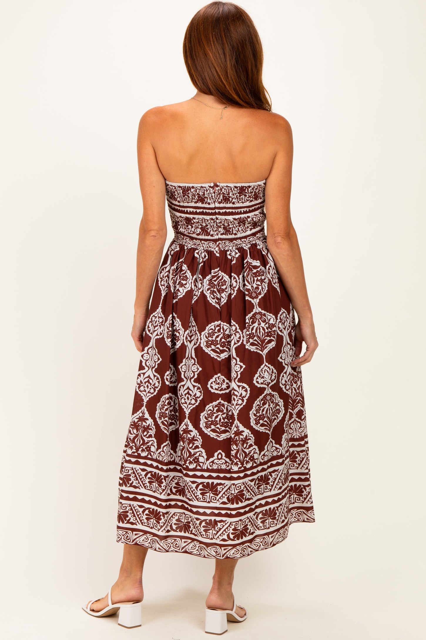 woman wearing a strapless brown and white patterned maxi dress with a fitted bodice and flowy skirt