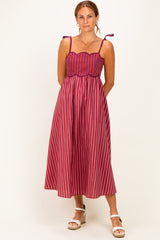 woman wearing a pink and red striped maxi dress with tie straps and a fitted bodice, standing against a neutral background