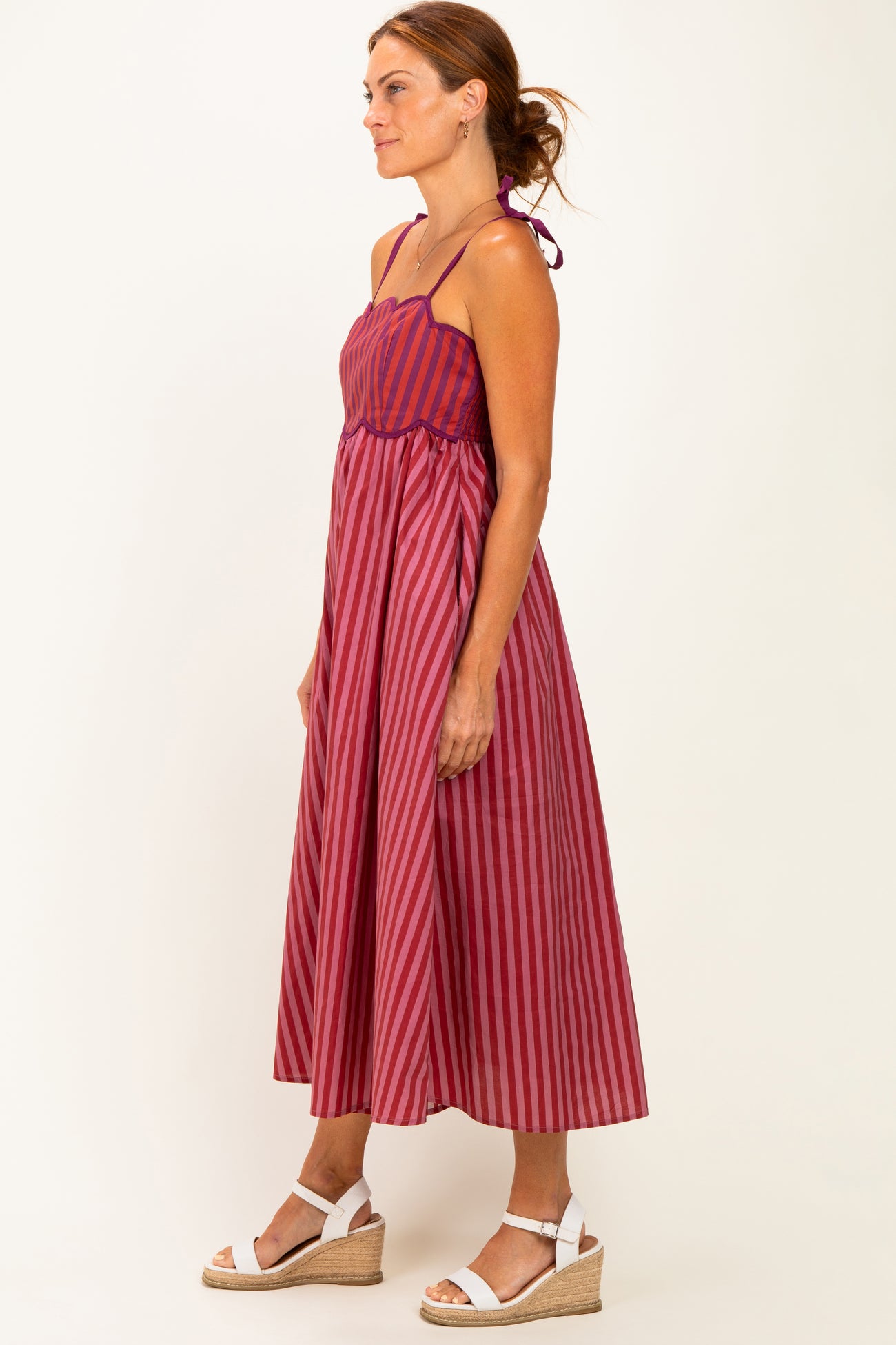 woman wearing a red and purple striped midi dress with spaghetti straps and a tie back detail
