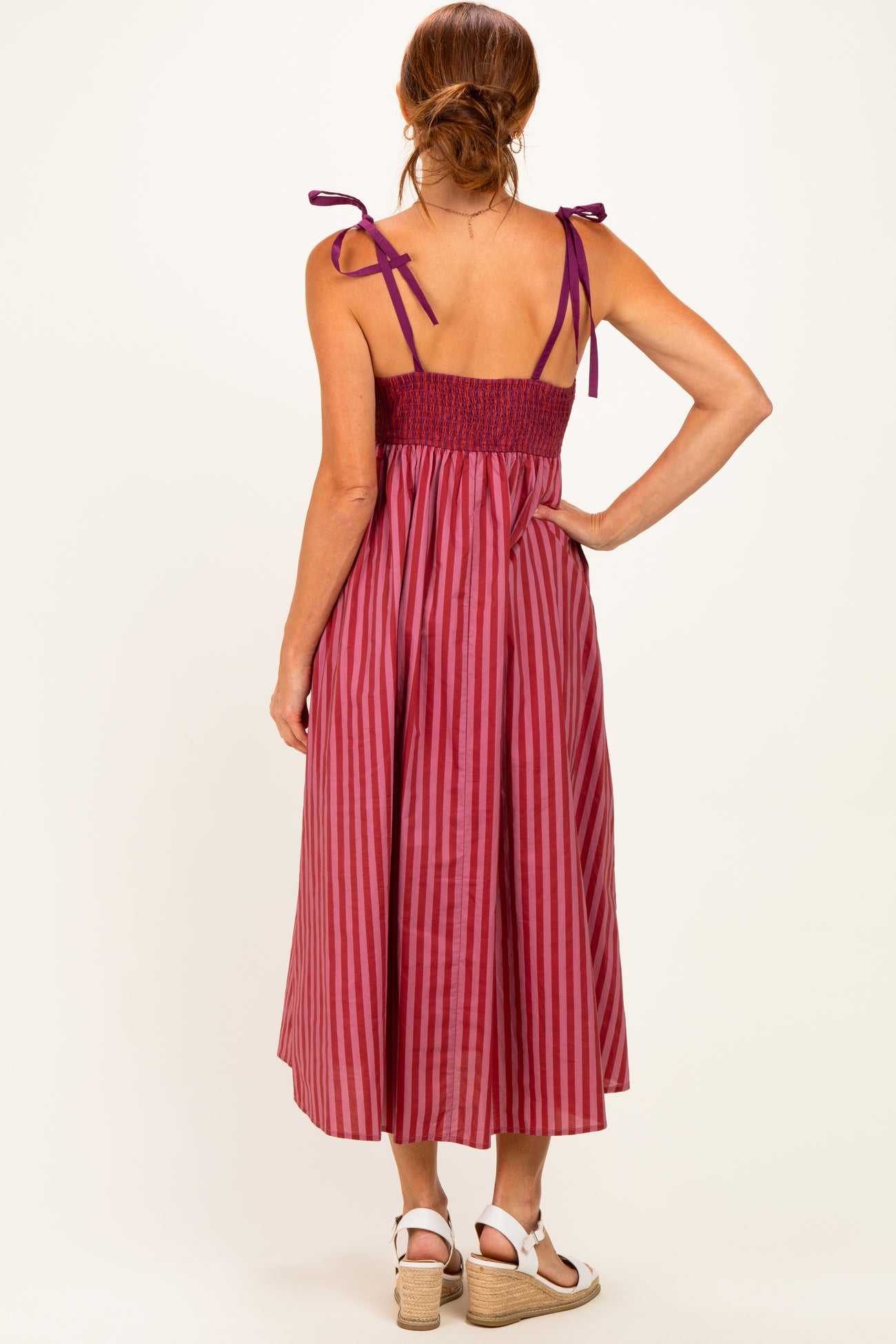 woman wearing a back view of a burgundy and pink striped maxi dress with tie shoulder straps