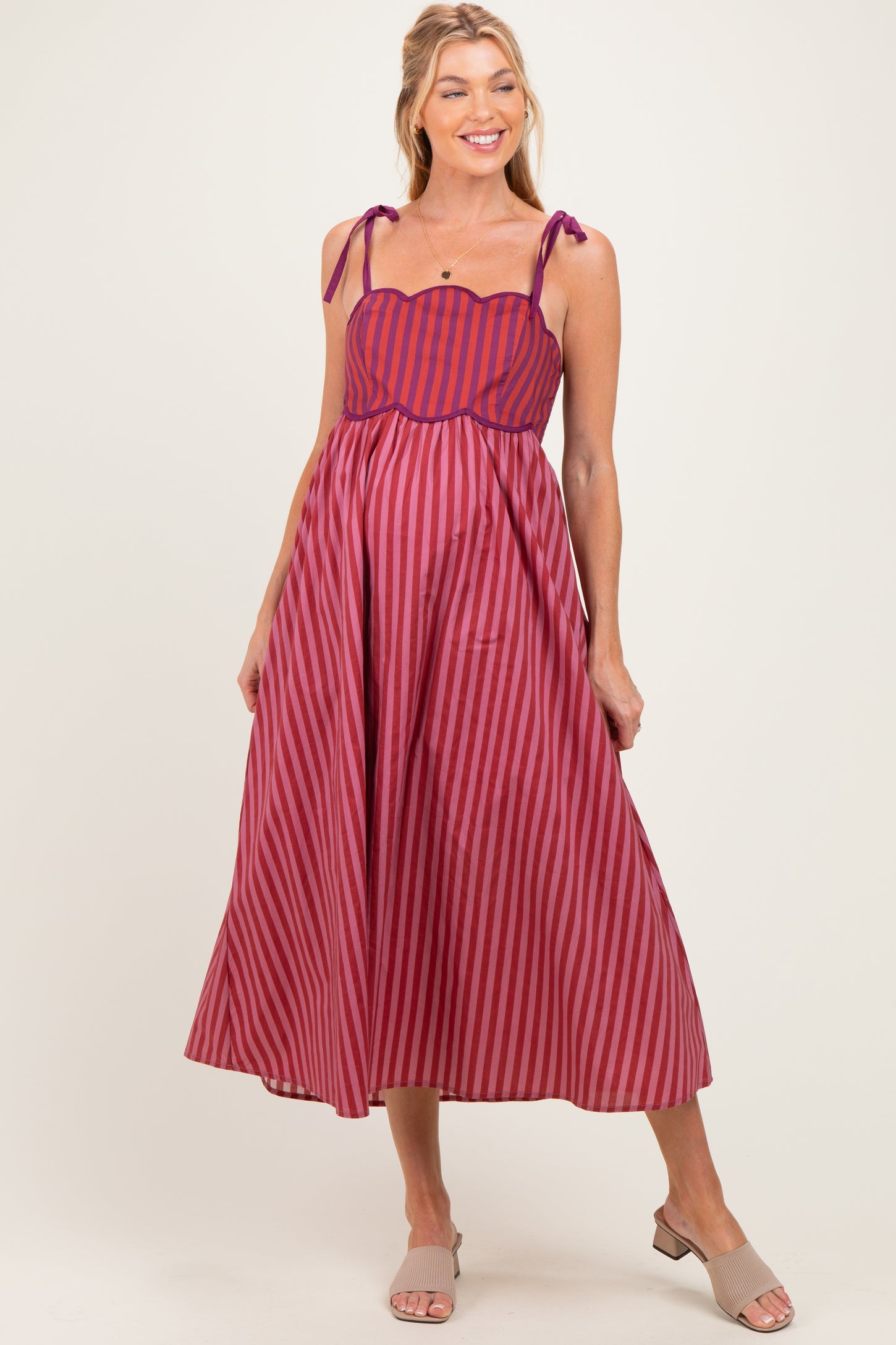 woman wearing a red and purple striped maternity dress with adjustable tie straps and a flowing skirt