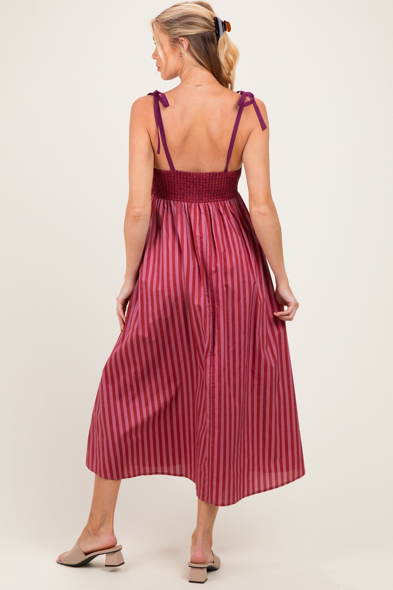 woman wearing a burgundy striped maternity dress with a smocked bodice and tie straps, showing her baby bump from the back