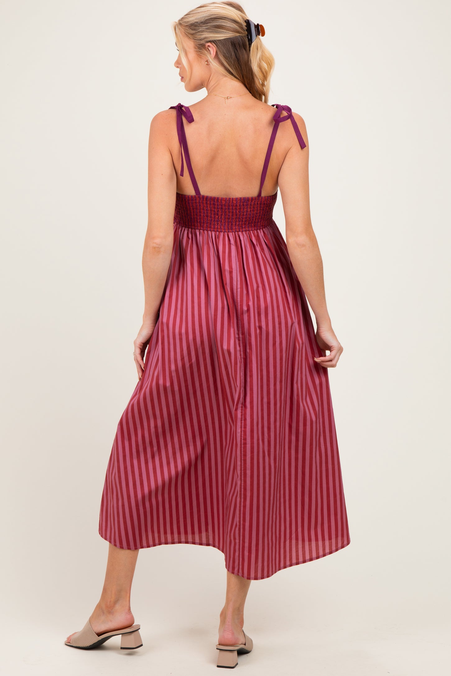 woman wearing a burgundy striped maternity dress with a smocked bodice and tie straps, showing her baby bump from the back