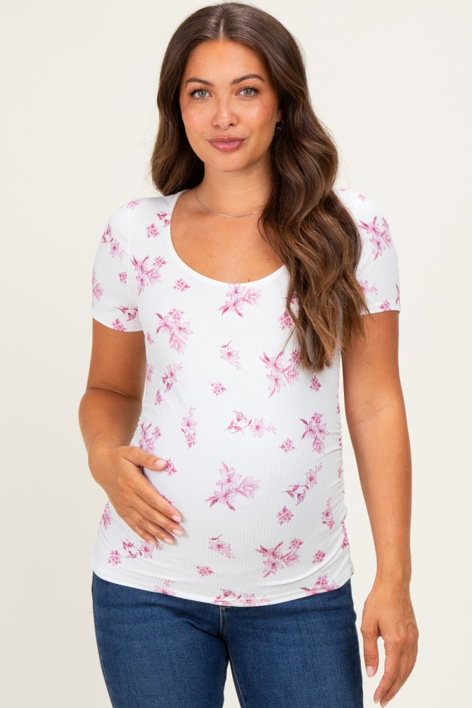 woman wearing a white maternity top with pink floral print and a scooped neckline, touching her baby bump