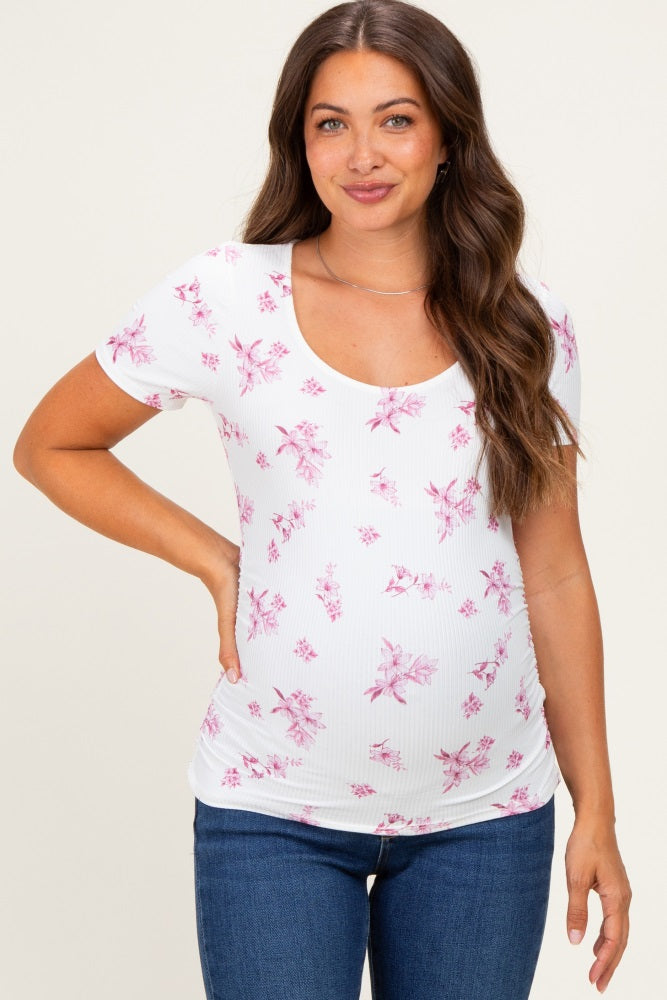 woman wearing a white maternity top with pink floral pattern and a scoop neckline, smiling and showing her baby bump