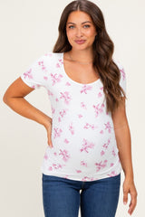 woman wearing a white maternity top with pink floral pattern and a scoop neckline, smiling and showing her baby bump