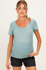 woman wearing a light green striped maternity top and showing her baby bump with a relaxed smile