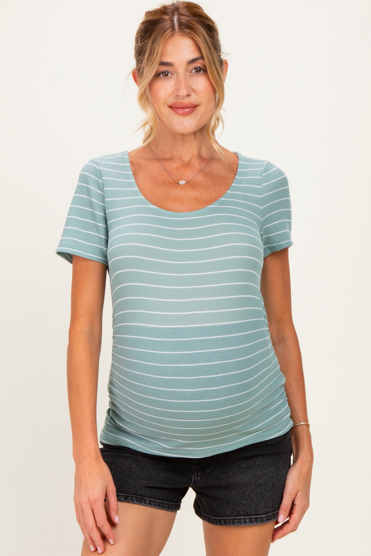 woman wearing a light green striped maternity top and showing her baby bump